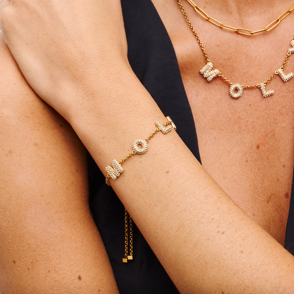 Gold bracelet with letter charms on a person's wrist against a black background